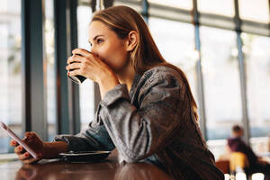 Frau in einem Restaurant trinkt Kaffee. Frau sitzt in einem Café mit Handy und trinkt eine Tasse Kaffee. - JLPSF14364