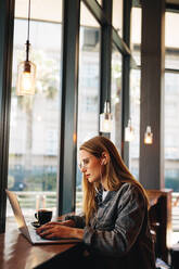Frau, die in einem Café am Laptop arbeitet. Frau mit Kopfhörern sitzt in einem Café und benutzt einen Laptop. - JLPSF14366