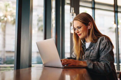 Frau sitzt an einem Cafétisch und arbeitet an einem Laptop. Frau surft im Internet auf einem Laptop mit Café Wifi. - JLPSF14367