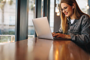Glückliche Frau arbeitet am Laptop, während sie in einem Café sitzt. Frau bereitet ihren Blog vor, während sie in einem Coffee Shop sitzt. - JLPSF14368