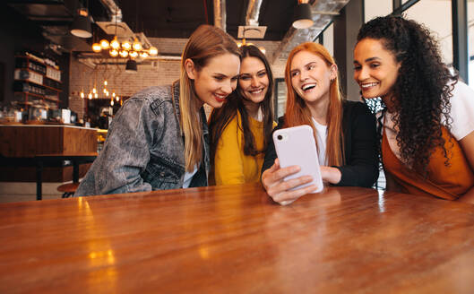 Eine Gruppe junger Frauen sitzt in einem Restaurant und schaut auf ein Mobiltelefon. - JLPSF14383