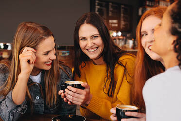 Frau mit einer Tasse Kaffee in der Hand sitzt mit Freunden in einem Café. Junge Frauen sitzen in einem Restaurant und trinken Kaffee. - JLPSF14389
