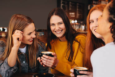 Woman holding a cup of coffee sitting with friends at a coffee shop. Young women sitting at a restaurant having coffee. - JLPSF14389