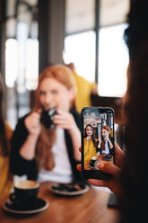 Female taking photograph of her friends making funny faces at a cafe. Woman taking photos of friends at a cafe. - JLPSF14392