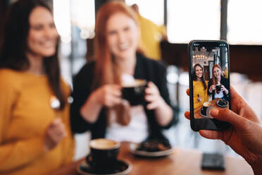 Friends having coffee being photographed with a call phone. Woman taking pictures of her friends in a cafe. - JLPSF14393