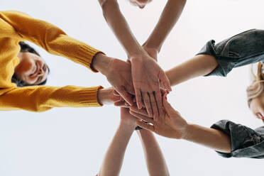 Tiefblickende Aufnahme einer Gruppe von Frauen, die einen Stapel Hände bilden, der Teamwork, Freundschaft und Einigkeit symbolisiert. - JLPSF14409