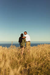 Rear view of a romantic couple standing together in a field. Portrait of a couple on holiday enjoying the beauty of nature. - JLPSF14419