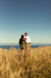 Rückansicht eines romantischen Paares, das zusammen in einem Feld steht. Porträt eines Paares im Urlaub, das die Schönheit der Natur genießt. - JLPSF14419