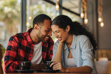 Romantisches Paar genießt das Zusammensein in einem Café. Afrikanischer Mann und Frau sitzen am Kaffeetisch und unterhalten sich lächelnd. - JLPSF14420