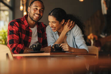 Verliebtes Paar bei einer Verabredung in einem Café. Afrikanischer Mann und Frau sitzen am Tisch eines Cafés und reden und lächeln. - JLPSF14424