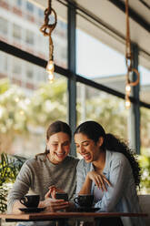 Zwei Frauen sitzen in einem Restaurant und schauen auf ihr Handy. Freunde sitzen in einem Café mit Kaffee auf dem Tisch und schauen auf ihr Handy. - JLPSF14427