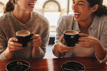 Zwei Frauen, die an einem Kaffeetisch sitzen und sich unterhalten und lachen. Glückliche Freundinnen in einem Café beim Kaffee trinken. - JLPSF14436