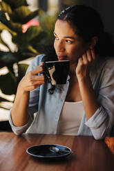 Afrikanische Frau sitzt im Café und trinkt Kaffee. Frau trinkt Kaffee im Café und schaut weg. - JLPSF14443