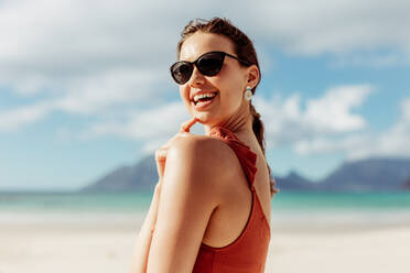 Porträt einer Frau, die am Strand steht und ihren Urlaub genießt. Fröhliche Touristin mit Sonnenbrille, die am Strand Spaß hat. - JLPSF14446