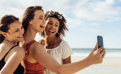 Cheerful woman on vacation taking selfie with friends on mobile phone for social media. Three women friends enjoying selfie at the beach. - JLPSF14454