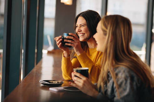 Two women having coffee and smiling. Happy female friends having a great time together in a cafe. - JLPSF14460