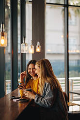 Fröhliche Freundinnen, die zusammen am Kaffeetisch sitzen. Lächelnde Frauen, die sich in einem Café treffen und plaudern. - JLPSF14464