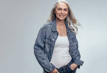 Stylish senior woman wearing casual denim shirt over grey background. Happy mature woman with cool style. - JLPSF14494