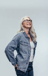 Stilvolle ältere Frau in casuals Blick auf Kopie Raum über grauen Hintergrund. Elegante Mitte erwachsenen kaukasischen Frau in Denim-Shirt und Brille wegschauen. - JLPSF14500