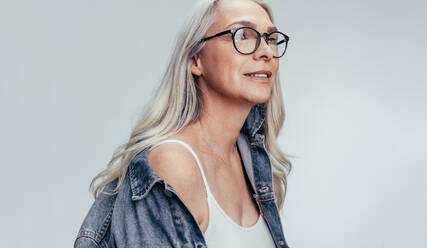 Schöne ältere Frau in casuals Blick auf Kopie Raum gegen grauen Hintergrund. Stilvolle Mitte erwachsenen kaukasischen Frau in Denim-Shirt und Brille wegschauen. - JLPSF14503