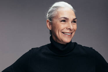 Lächelnde ältere Frau, die ein schwarzes T-Shirt trägt und wegschaut. Mittlere erwachsene kaukasische Frau in Freizeitkleidung auf grauem Hintergrund. - JLPSF14517