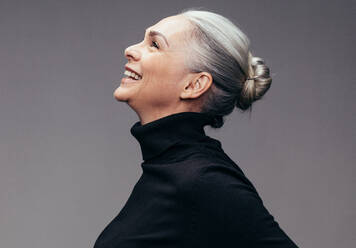 Seitenansicht einer lachenden älteren Frau auf grauem Hintergrund. Profilansicht einer reifen Frau in schwarzer Freizeitkleidung, die glücklich aussieht - JLPSF14522