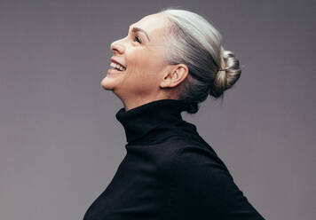 Side view of senior woman laughing on gray background. Profile view of mature woman in black casuals looking happy - JLPSF14522