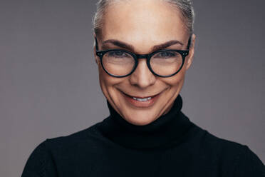 Mid Erwachsene kaukasische Frau in T-Shirt und Brille lächelnd auf grauem Hintergrund. Positive reife Frau in Casuals lächelnd in die Kamera. - JLPSF14525