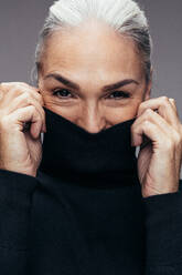 Close up of happy mature woman covering her face with t-shirt. Senior woman feeling cold. - JLPSF14528