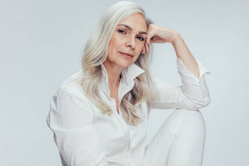 Senior woman sitting over white background. Mature caucasian woman sitting relaxed in studio with her hand on head. - JLPSF14537