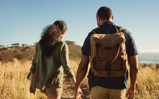 Couple on a hiking trip on a sunny day. Rear view of a couple walking together on a hiking trail. - JLPSF14601