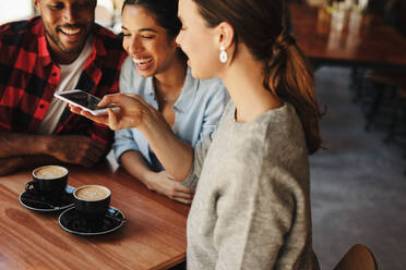 Frau, die mit ihrem Smartphone Fotos von Kaffee macht, während sie mit ihren Freunden in einem Café sitzt. - JLPSF14623