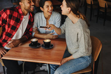 Eine Frau fotografiert mit ihrem Handy einen Kaffee in einem Café mit Freunden. Eine Gruppe von Freunden trifft sich in einem Café und fotografiert mit ihrem Handy einen Kaffee. - JLPSF14624