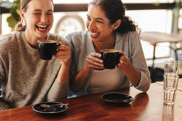 Zwei Frauen, die an einem Kaffeetisch sitzen und sich unterhalten und lachen. - JLPSF14626