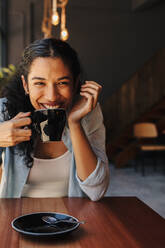 Schöne Frau trinkt eine heiße Tasse Kaffee in einem Café. Lächelnde Frau trinkt Kaffee in einem Café. - JLPSF14629