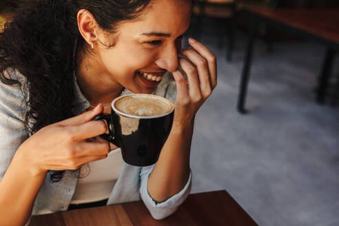 Closeup of a female holding cup of coffee and smiling. Woman sitting in a coffee shop smiling with her cup of coffee. - JLPSF14631