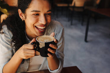 Frau mit einer Tasse Kaffee in einem Café sitzend. Nahaufnahme einer afrikanischen Frau, die Kaffee trinkt und lächelt. - JLPSF14632