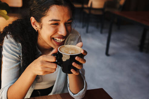 Woman holding a cup of coffee with both hands while sitting at cafe. Smiling woman having coffee at a restaurant. - JLPSF14633