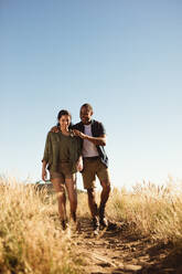 Ein Paar genießt seine Wanderung auf einem Hügel. Ein lächelndes Paar, das gemeinsam auf einem felsigen Pfad spazieren geht. - JLPSF14655