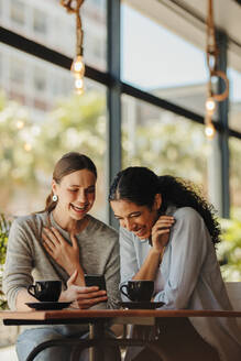 Freunde treffen sich in einem Café und schauen auf ihr Handy. Eine Frau zeigt ihrem Freund das Handy und lächelt. - JLPSF14665