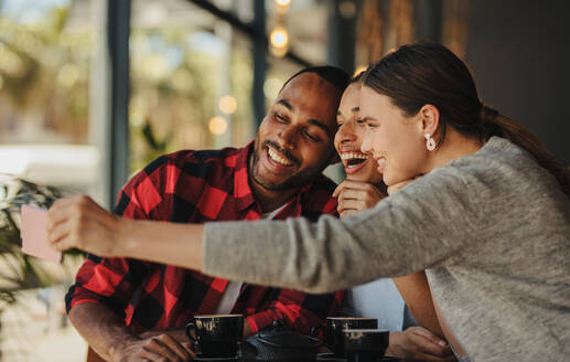 Eine Gruppe von Freunden macht ein Selfie in einem Café. Ein multiethnischer Mann und eine Frau in einem Café machen ein Selfie mit ihrem Mobiltelefon. - JLPSF14670