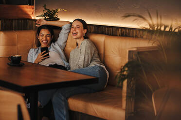 Glückliche Freundinnen in einem Café an einem Wochenende. Zwei Frauen sitzen an einem Kaffeetisch und lächeln. - JLPSF14674