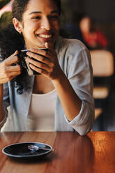 Frau mit einer Tasse Kaffee in einem Café sitzend. Nahaufnahme einer afrikanischen Frau, die Kaffee trinkt und lächelt. - JLPSF14676