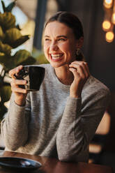Eine Frau hält eine Tasse Kaffee in der Hand und lächelt. Fröhliche Frau sitzt in einem Café und trinkt Kaffee. - JLPSF14678