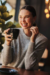 Female holding cup of coffee and smiling. Cheerful woman sitting in a coffee shop drinking coffee. - JLPSF14678