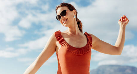 Porträt einer lächelnden Frau in spielerischer Stimmung im Freien stehend. Nahaufnahme einer fröhlichen jungen Frau mit Sonnenbrille, die ihren Urlaub genießt. - JLPSF14681
