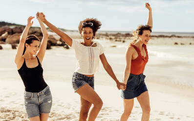 Junge Frauen, die spielerisch am Strand spazieren gehen. Multiethnische Frauen, die sich im Strandurlaub amüsieren. - JLPSF14682
