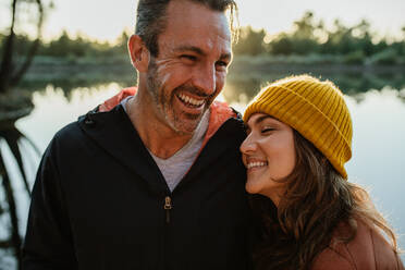 Verliebtes Paar steht an einem See im Wald und lacht. Lächelnder Mann und lächelnde Frau auf einem Campingausflug. - JLPSF14687
