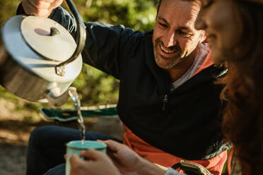 Ein Paar trinkt Kaffee beim Camping in der Natur. Ein Mann gießt Kaffee in die Tasse der Frau. - JLPSF14694