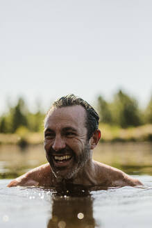 Lächelnder reifer Mann, der in einem See schwimmt. Gesicht eines mittleren erwachsenen Mannes über der Wasseroberfläche, der wegschaut und lächelt. - JLPSF14722